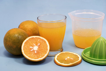 a glass of sweet orange juice with orange slices and squeezer isolated on blue