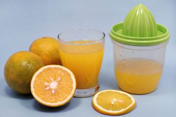 a glass of sweet orange juice with orange slices and squeezer isolated on blue