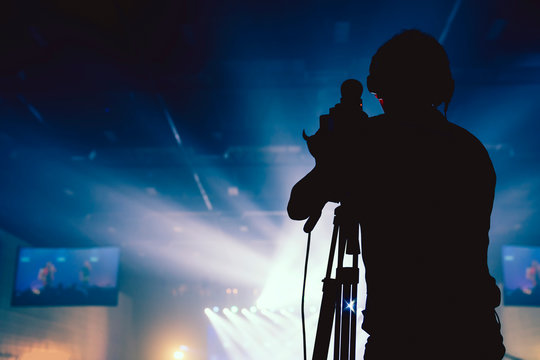 silhouette camera man standing record live concert with smoke and light performance background