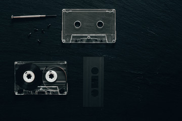 Minimalist flat lay of opened retro cassette with small screwdriver on black background with copy space - Vintage audio device used to record music on it - old fashioned plastic tape