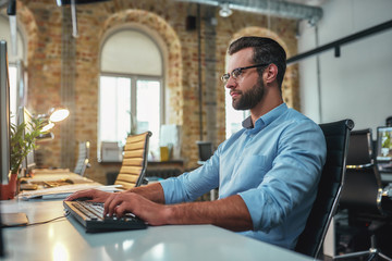 Fototapeta premium Successful businessman. Young bearded man in eyeglasses and formal wear working on computer while sitting in the modern office