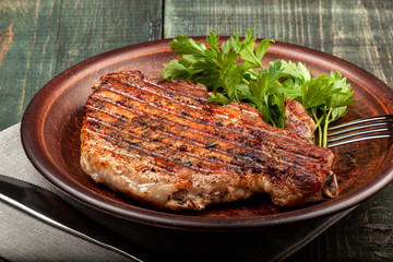 a piece of fried pork with herbs on a white dish on a wooden table, closeup view