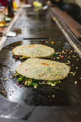Okonomiyaki, Japanese pancake in the making. Tasty traditional dish from Hiroshima prefecture, Japan.