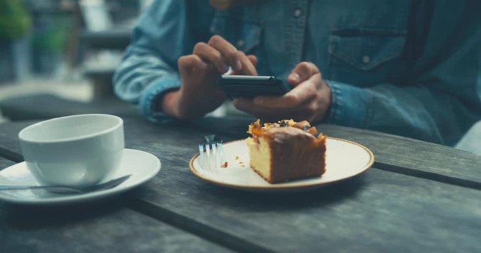 Young woman eating cake and drinking coffee whilst using phone