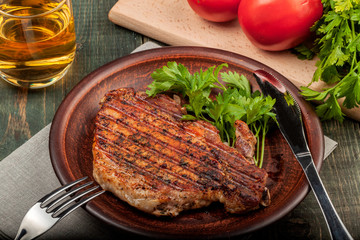 a piece of fried pork with herbs on a white dish on a wooden table, closeup view