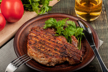 a piece of fried pork with herbs on a white dish on a wooden table, closeup view