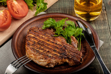 a piece of fried pork with herbs on a white dish on a wooden table, closeup view