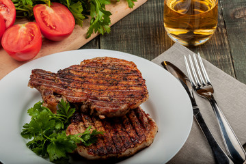 a piece of fried pork with herbs on a white dish on a wooden table, closeup view