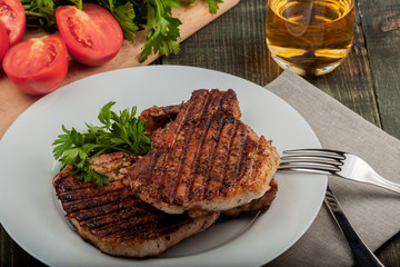 a piece of fried pork with herbs on a white dish on a wooden table, closeup view