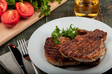 a piece of fried pork with herbs on a white dish on a wooden table, closeup view