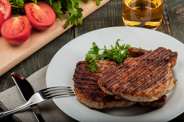 a piece of fried pork with herbs on a white dish on a wooden table, closeup view