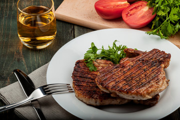 a piece of fried pork with herbs on a white dish on a wooden table, closeup view