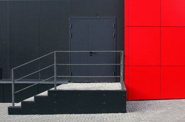 Emergency exit of the modern industry building. Black wall, black door, red wall and staircase with railing.