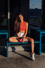 Stylish happy young brunette woman wearing white shorts and sneakers holding pink cup of coffee to go.