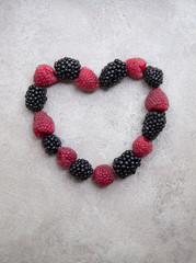 Fresh ripe blackberries and raspberries folded in the shape of aheart on light background.Top view.
