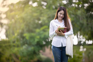 Happy woman student on the park and writing something on notebook, Education concept