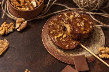 Slices of apples in chocolate, caramel glaze and walnuts on skewers on a dark background