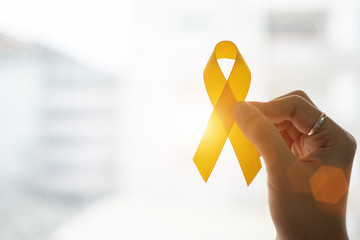 Suicide prevention and Childhood Cancer Awareness, Yellow Ribbon on wooden background  for supporting people living and illness. children Healthcare and World cancer day concept - obrazy, fototapety, plakaty