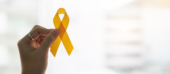 Suicide prevention and Childhood Cancer Awareness, Yellow Ribbon on wooden background  for supporting people living and illness. children Healthcare and World cancer day concept