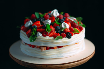Fruit cake. Cake decorated with berries on a wooden stand on a black background.