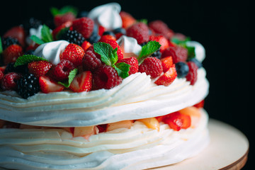 Fruit cake. Cake decorated with berries on a wooden stand on a black background.