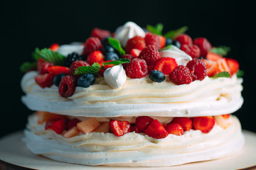 Fruit cake. Cake decorated with berries on a wooden stand on a black background.