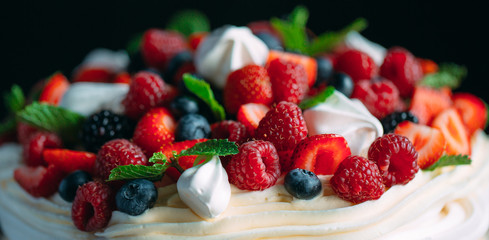 Fruit cake. Cake decorated with berries on a wooden stand on a black background.