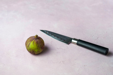 Knife and fresh whole fig on a light pink marbled background with copy space. Selected focus