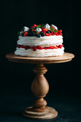 Fruit cake. Cake decorated with berries on a wooden stand on a black background.