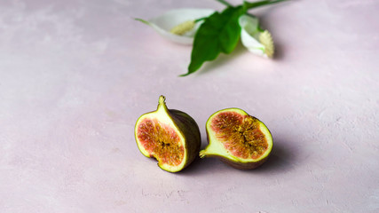 fresh whole and cut figs with some flowers on a light pink marbled background with copy space. Selected focus