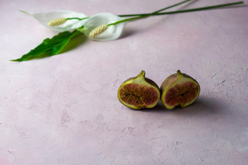 fresh whole and cut figs with some flowers on a light pink marbled background with copy space. Selected focus