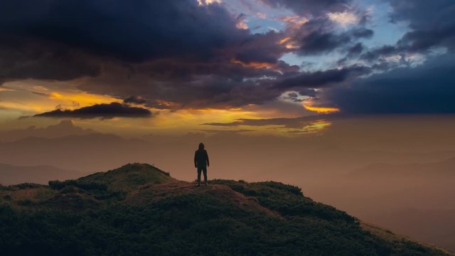 The man standing on a mountain against a picturesque cloud stream. time lapse
