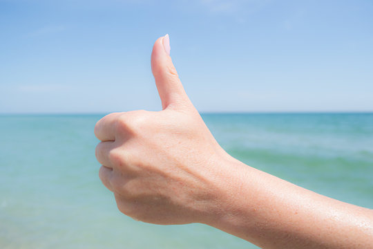 Sign with thumb up. Female hand against the sky and blue sea