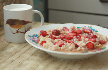 Homemade oatmeal with strawberries and a cup of milk.