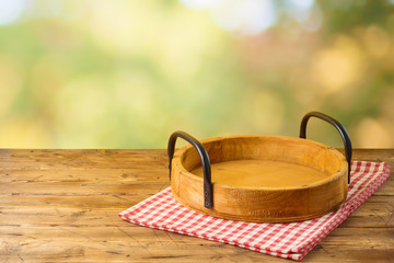 Empty wooden tray with red checked tablecloth on wooden table over autumn bokeh background