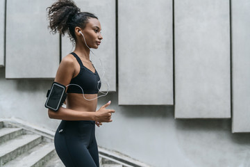 Young woman with earphones running on the steps as exercising outdoors in city