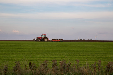 Roter Trecker pl&uuml;gt  gr&uuml;nes Feld mit blauem Himmel