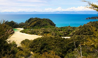 View beyond tree branches on bay with white sandbank turquoise water, green hills and blue ocean background - Abel Tasman national park, New Zealand