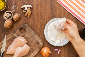 Raw fillet. Cooking Chicken. Breading with flourby hand, starch and spices. Lemon, fresh champignons, onions, garlic, wine, salt and olive oil. Wooden cutting board. Top layout