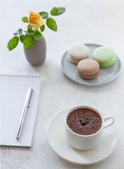 cup of hot chocolate with macarons flowers and notepad on a white background