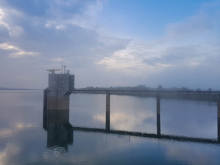 Dam Flood control building at full reservoir in the morning mist on the background of the sky
