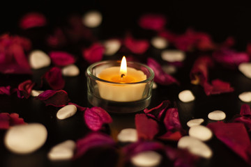 burning candle with red rose petals and marble stones on black background	