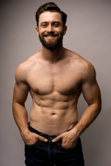 Handsome young man on white background looking at camera. Portrait of laughing young man with hands in pockets. Happy topless guy smiling.