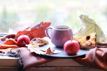 Naklejka na ściany i meble Cup of coffee on the background of the window, behind which rain, apples, a warm scarf, leaves, autumn season, the concept of home comfort