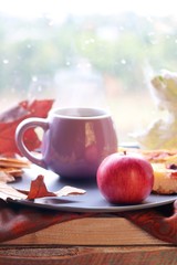 Cup of coffee on the background of the window, behind which rain, apples, a warm scarf, leaves, autumn season, the concept of home comfort
