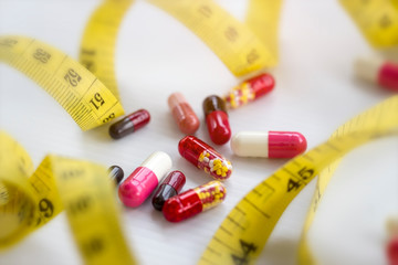 Diet concept; Slim with pills, dangerous for health. Pills, capsule with measuring tape on white background.
