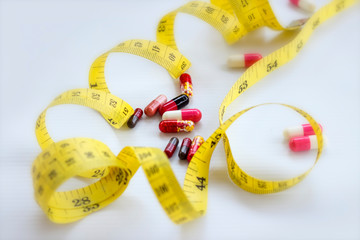 Diet concept; Slim with pills, dangerous for health. Pills, capsule with measuring tape on white background.