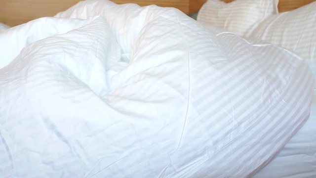 A little boy plays with his mother in bed in the morning, the mother covers the child with a blanket. Happy family having fun in the bedroom on the bed. Slow motion.