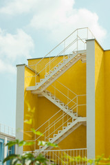 Modern yellow and white house with metal zigzag staircase. Courtyard of a building, beautification.