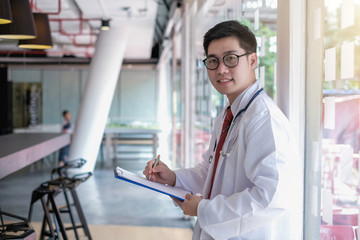 Male doctor stand holding the clipboard in his office. Look at the camera.